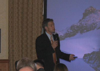Presenter speaking at conference with mountain backdrop