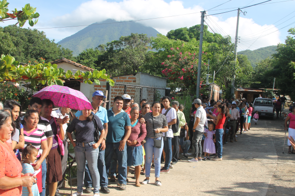 People lined up on a sunny street near mountain.