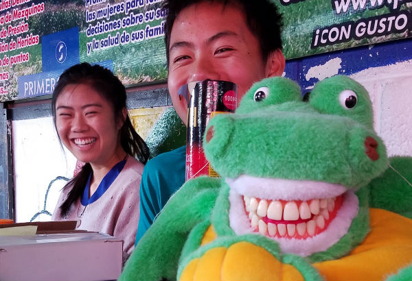 People smiling behind a green plush toy.