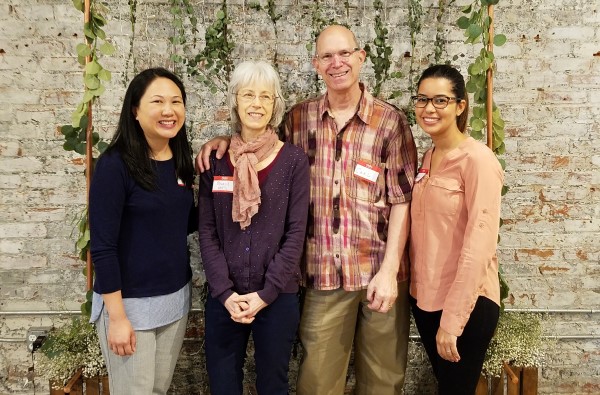 Four people smiling in front of a plant wall.